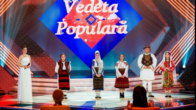 Cu un picior în ţară şi altul afară, cântă la „Vedeta populară”